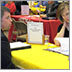 Photo of a man and a woman sitting at a table interviewing another man sitting across the table from them at a job fair.