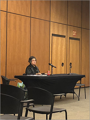 Photo of Donna Jodhan sitting at a table in front of a microphone with an ear piece in.