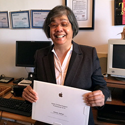 Donna Jodhan smiling while holding her Apple Certified Support Professional (ACSP) Certificate.